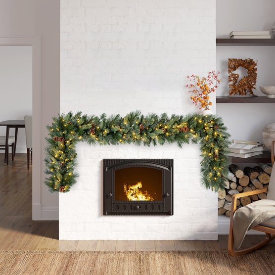 Pre-lit Greenery Garland with Pine Cones Across a White Brick Fireplace — Christmas Lights in Garland Indoor