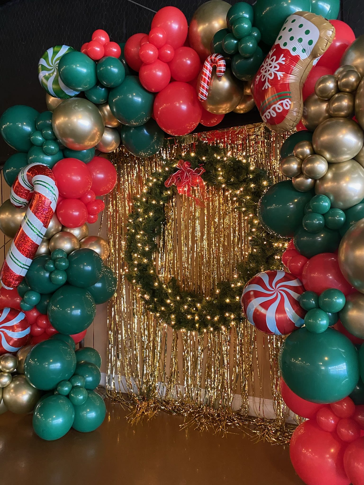 Christmas Balloon Garland Arch Framing a Wreath with Tinsel Backdrop Christmas Balloon Garland Arch Framing a Wreath with Tinsel Backdrop