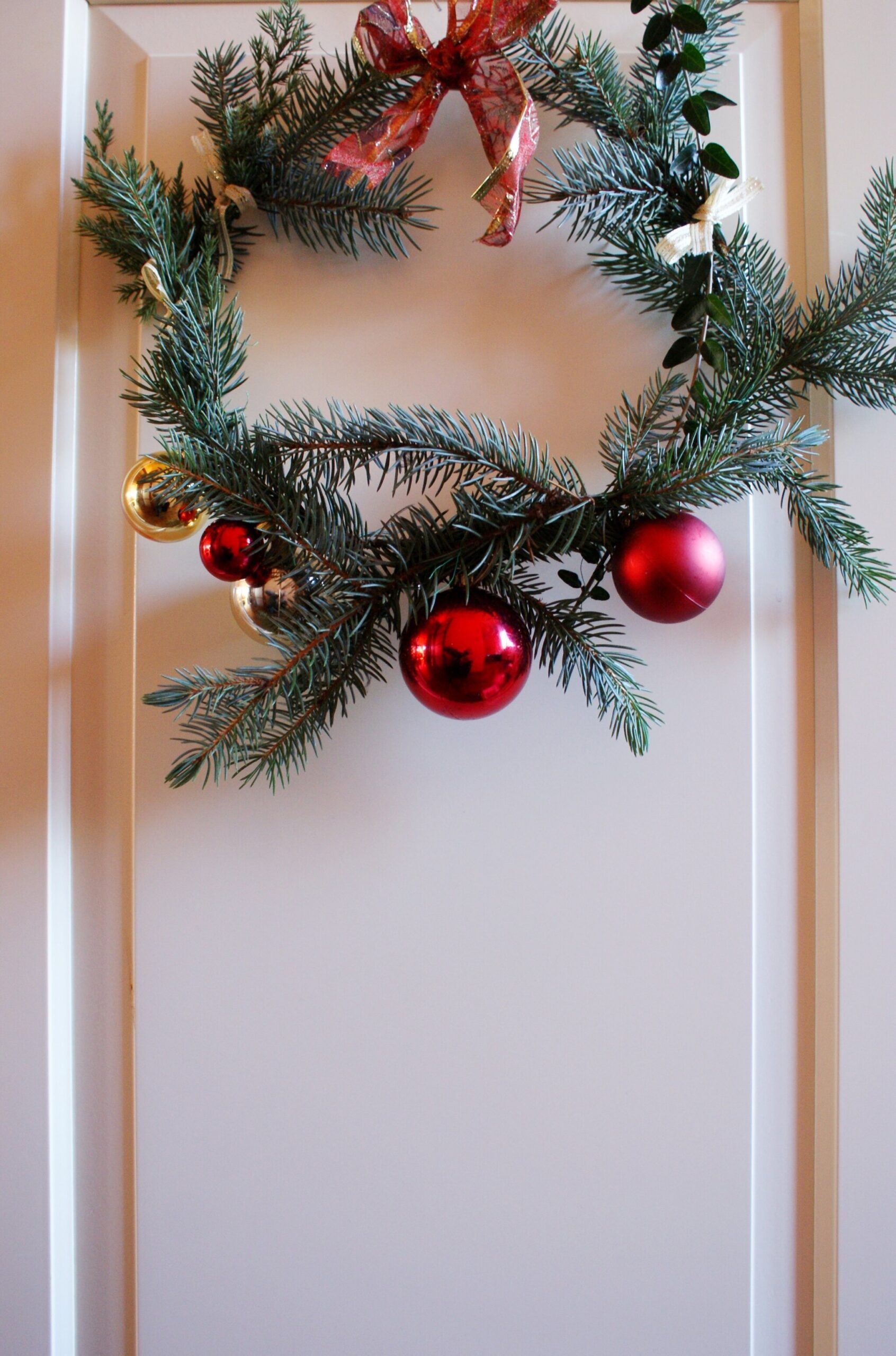 Simple Pine Wreath with Red Baubles and Gold Accents on a White Door — DIY Christmas Wreath