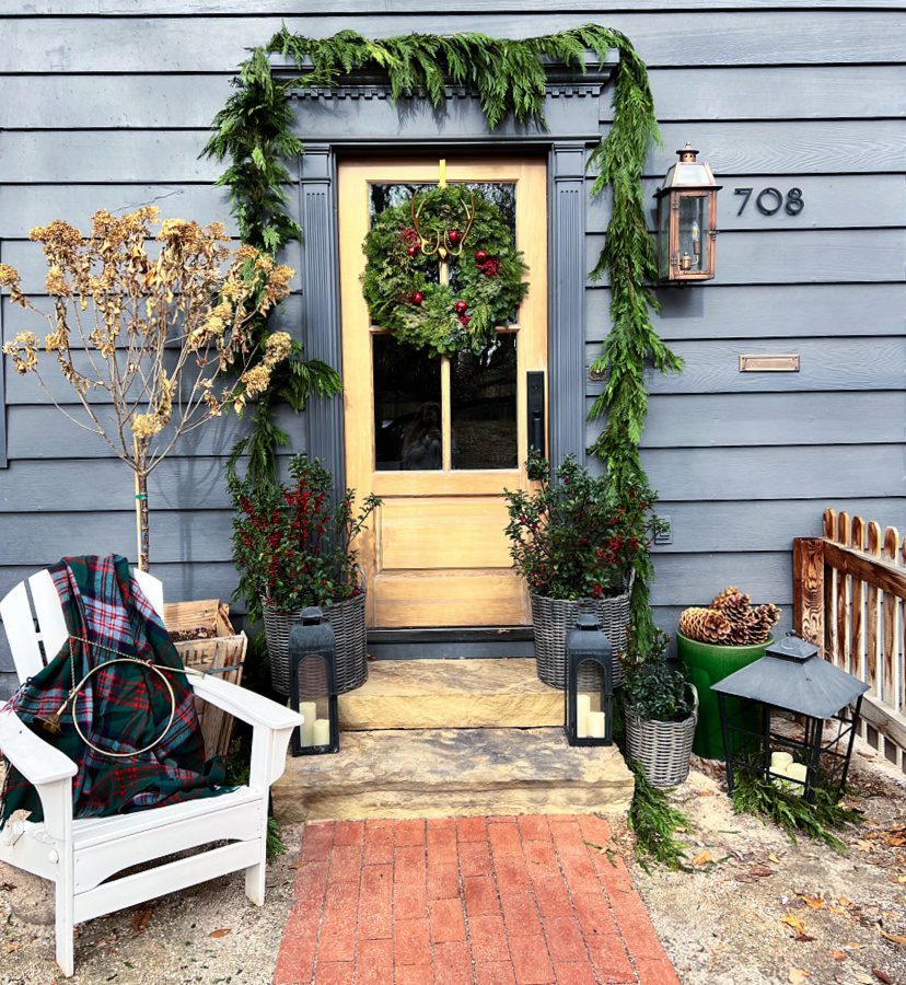 Natural Wood Door Framed by Lush Pine Garland and Plaid Blanket — Farmhouse Christmas Porch