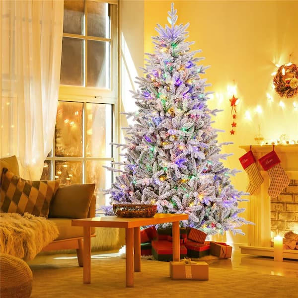 Full Flocked Artificial Tree with Vibrant Multicolor Lights Near Fireplace Full Flocked Artificial Tree with Vibrant Multicolor Lights Near Fireplace — Christmas Tree with Colored Lights