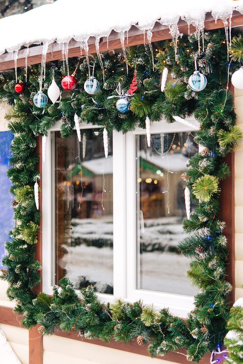 Window Framed by Dense Evergreen Garland with Ornaments and Icicles Window Framed by Dense Evergreen Garland with Ornaments and Icicles — Christmas Window Decor Outdoor